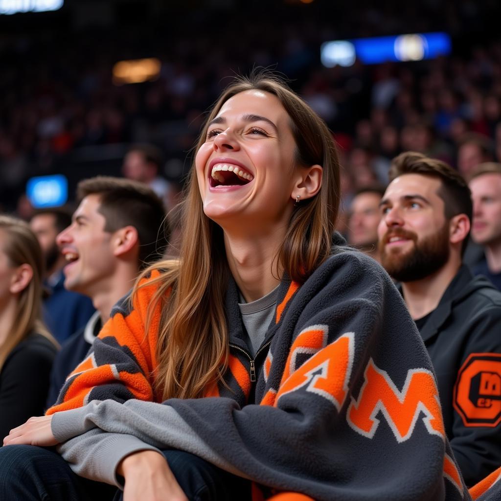 A basketball fan, beaming with joy, is comfortably wrapped in a fleece blanket showcasing their favorite team's colors and logo, while watching a game on TV.