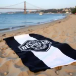 Black and white striped Beşiktaş beach towel spread out on a sandy beach with the Bosphorus Bridge in the background