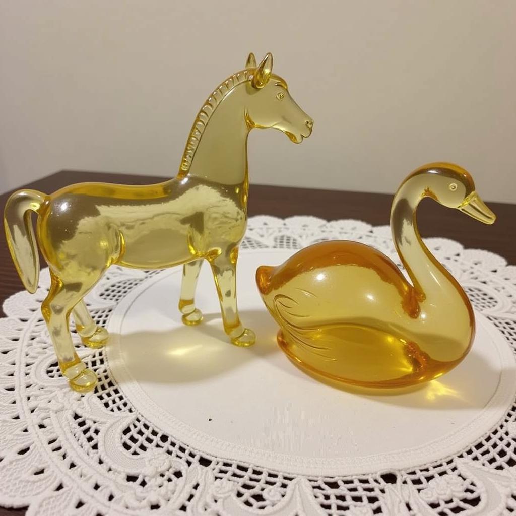 Two vintage clear glass animal figurines, a horse and a swan, displayed on a table with a lace doily