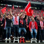 Beşiktaş fans chanting, waving flags, and standing on stools in the stadium.